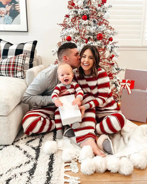 Family in matching striped pajamas sitting in front of a decorated Christmas tree.