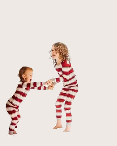 Two children in matching red and white striped pajamas standing in a room with a Christmas tree.