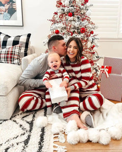 Family in matching striped pajamas sitting in front of a decorated Christmas tree.