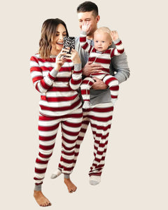 Family of three wearing matching red and white striped pajamas in a living room.